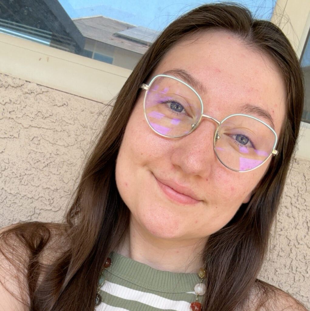 person with glasses and long straight brown hair looking at the camera and smiling.